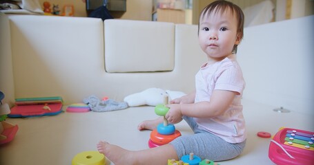 child toddler girl is playing with a stack of colorful blocks. The blocks are arranged in a pyramid shape sitting on the floor, reaching for them. Concept of curiosity and exploration