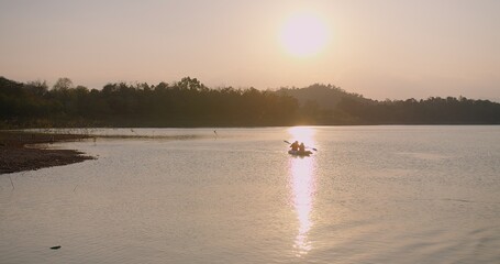 Kayakers enjoy a serene sunset paddle a kayak on a calm lake with a golden path reflecting on the water at sunset. The water is calm and the sky is orange