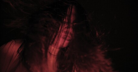 A woman ghost with hair over their face with wind blowing illuminated by a red light creating a...