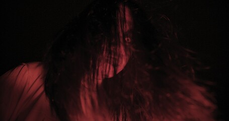 A woman ghost with hair over their face with wind blowing illuminated by a red light creating a...