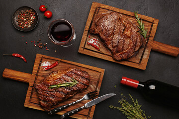 Striploin and Ribeye grilled beef steaks served on wooden boards with glass of wine, bottle of...