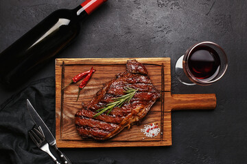 Striploin grilled beef steak served with rosemary, salt and peppercorns on wooden board with glass...