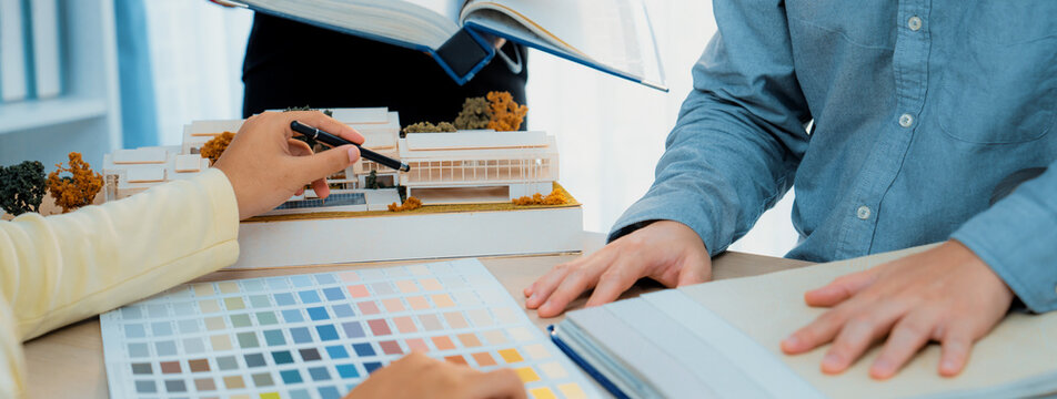 Cropped image of professional interior design team discuss about color and material usage for the project while project manager choose main theme color with house model on meeting table. Variegated.