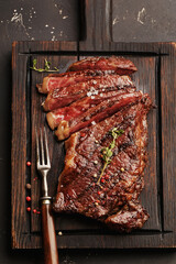 Medium rare sliced grilled striploin beef steak served on wooden board with vintage fork, salt,...