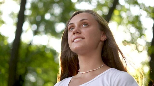 beautiful girl smiling. inner beauty and love for nature concept. beautiful woman stands in a park outdoors in a white T-shirt and smiles, face close-up, lifestyle sun glare on the background