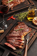 Medium rare sliced grilled striploin beef steak served on wooden board with vintage fork, glass of...