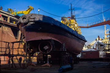 Fishing vessel maintenance in shipyard drydock. Workers repair, repaint hull, propeller, docked...