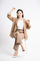 Full body image of young Asian businesswoman sitting and posing on white background