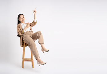 Full body image of young Asian businesswoman sitting and posing on white background
