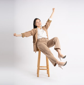 Full body image of young Asian businesswoman sitting and posing on white background
