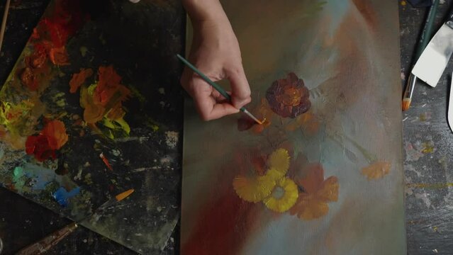 Close-up, artist's hand drawing a picture with flowers with oil paints in art studio