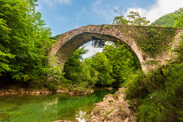 Fototapeta na wymiar Old bridge over the Dobra river, dating from the Middle Ages and built on the remains of an old Roman road, between the municipalities of Cangas de Onis and Amieva, Asturias.