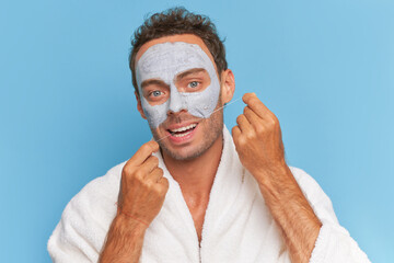 Close-up of young man brushes teeth with dental floss and applys cosmetics clay mask on his face, spa treatments concept, copy space