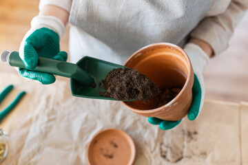 people, gardening and planting concept - close up of woman in gloves with trowel pouring soil to flower pot at home - 759998501