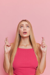 Closeup shot of pretty girl with long fair hair in pink top standing on pink background pointing up, good choice concept, copy space
