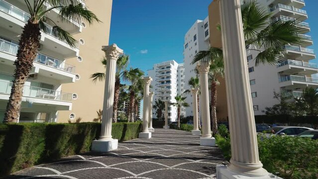 Luxury apartment complex with palm-lined pathway, sunny weather, high-rise living, upscale residential buildings, urban landscape, modern lifestyle