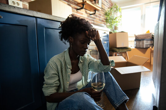 Woman sitting on the floor with wine looking stressed during moving