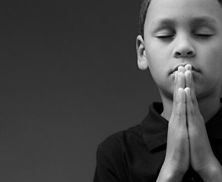 boy praying to God with hands together on grey black background with people stock image stock photo