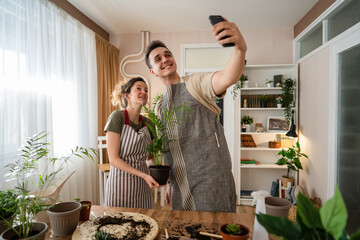 Couple caucasian man and woman wife and husband planting flowers together taking care of home plants real people domestic life family gardening concept take selfie photo with smartphone copy space