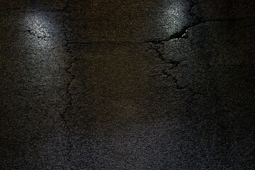 Cracks in the asphalt at night, illuminated by car lights.