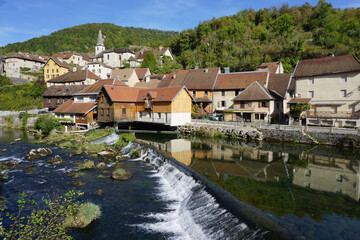 Fototapeta na wymiar small village by the river with waterfall and mirror reflection in eastern france