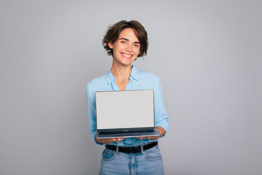 Close up image of smiling beautiful modern business woman in smart casual wear shows laptop in hands with blank screen. Copy space for your apps and adverts your firm
