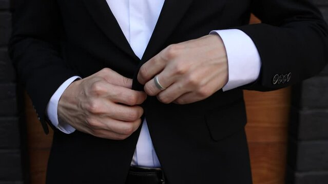 a man in a black suit fastens the button of his jacket