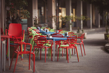Fototapeta na wymiar A street cafe in the street of Recco, Italy. Empty stylish street cafes. ready for the tourist season. Restaurant with colorful furniture is on the foreground.