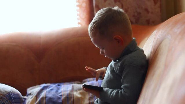 Little boy, child playing on mobile device, phone at home close up