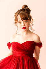 Young woman in red dress striking a pose for a picture, showcasing elegance and confidence. Isolated. Studio shot.