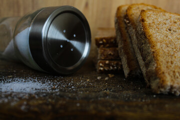 Slices of whole wheat bread on the bread cutting board and salt shaker and salt on the floor