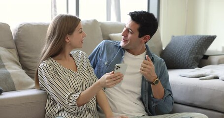 Surprised millennial Hispanic wife and husband sit in living room with smart phone, read happy news on sms. Moment of online lottery win, bank mortgage approval, new job opportunities for young couple