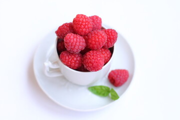Lots of raspberries in a white rustic cup, green basil leaf on a white background isolated. Fresh ripe summer berries on a plate. Close. up