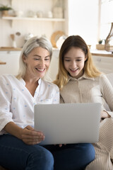 Positive preteen girl relax at home with mature mother, look at laptop screen, watch movie or...
