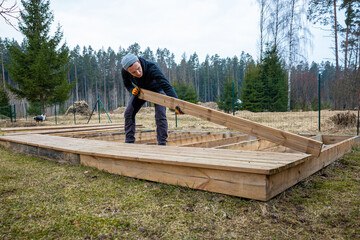 man constructing a wooden deck or terrace in a rural outdoor setting, demonstrating diy carpentry skills and home improvement