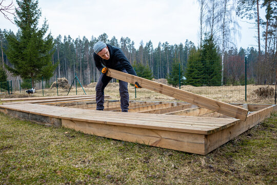 man constructing a wooden deck or terrace in a rural outdoor setting, demonstrating diy carpentry skills and home improvement