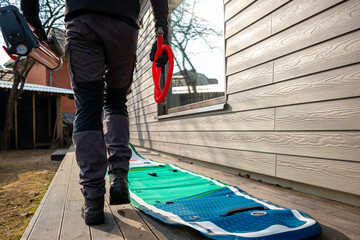 Man with a paddle and inflating an SUP board on a wooden deck near a house