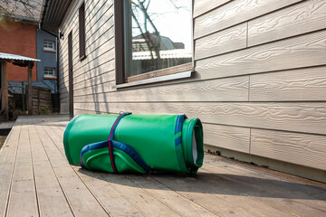 Green Inflatable Stand-Up Paddle Board Rolled Up Next to Wooden House Ready for Summer Fun