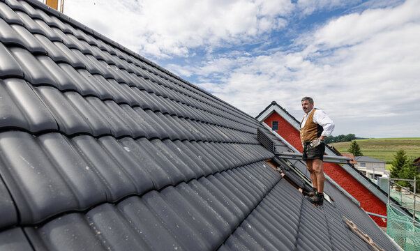 roofer in traditional German clothing of a craftsman working with roof tiles on the roof.
