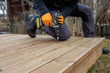 Deck or terrace construction, builder hand with electric screwdriver installing impregnated wooden...