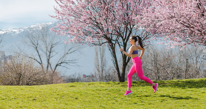 Sportive girl running in park on spring day in front of blossom