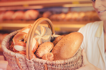 sales woman in bakery shop presenting a basket with bread and rolls - 760059571