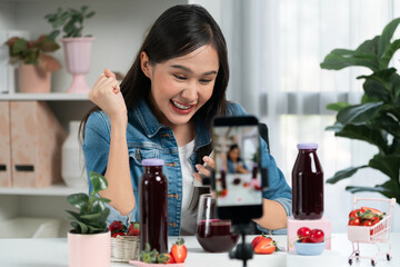 Smiling young beautiful Asian reviewing tasty mixed strawberry and cherry juice detox drinks,...