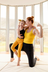 Fototapeta na wymiar Young fit mom and her daughter in matching clothes, showing muscles.