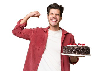 Young caucasian man holding birthday cake over isolated background doing strong gesture