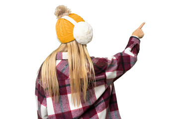 Young pretty blonde woman wearing winter muffs over isolated chroma key background pointing back...