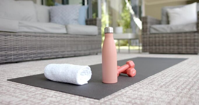 A yoga mat hosts a water bottle, towel, and dumbbells