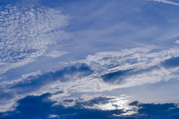 Niebo lekko zachmurzone, częściowo pokryte białymi chmurami, zza których widać błękit nieboskłonu. - obrazy, fototapety, plakaty