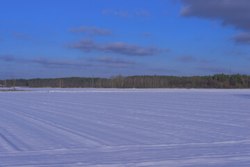 Zimowy, słoneczny dzień. Równina pokryta polami uprawnymi i łąkami pokryta jest warstwą śniegu. - obrazy, fototapety, plakaty