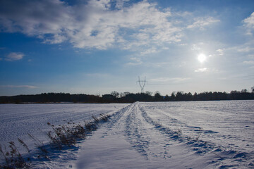 Zimowy, słoneczny dzień. Równina pokryta polami uprawnymi i łąkami pokryta jest warstwą śniegu.